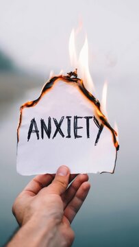 Hand holding burning paper with word ANXIETY for mental health treatment psychology therapy self help blog emotional support overcoming fear burning away stress release of tension transformation mood 