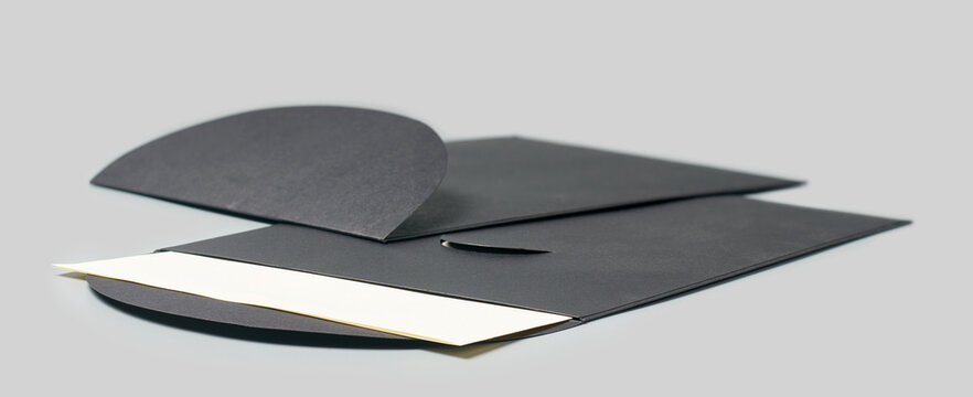 two matte black paper envelopes with blank white card partially tucked inside on grey background, side view with soft focus, elegant premium mailing concept