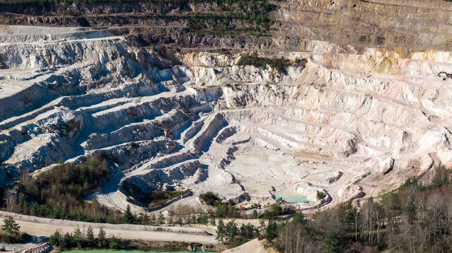Aerial view of the stark white quarry's terraced levels contrasting with the surrounding green trees, Echassieres, Auvergne-Rhone-Alpes, France.