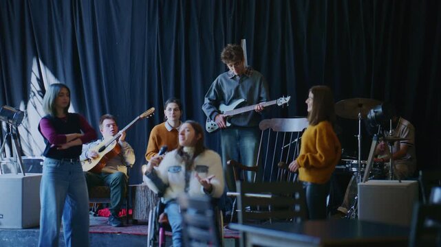 A diverse group of young students collaborates on music, practicing with various instruments and vocals. This inclusive student band performs together in a creative rehearsal setting.