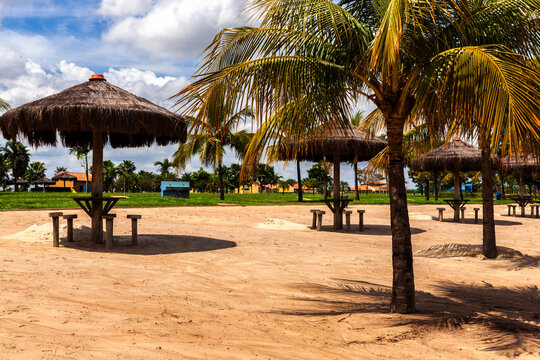 A sunny day at a river beach in Gustavo Simioni Ecological Park. Thatched umbrellas and tables on the sand create a perfect spot for leisure and tourism.