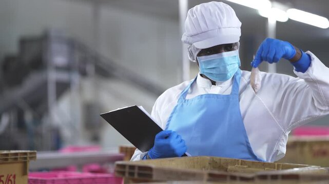 food safety researchers in lab coats discussing quality audit findings in seafood processing facility. A food safety inspector holding a clipboard while overseeing factory workers processing seafood