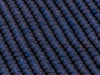Fototapeta premium Close-up of dark blue ceramic roof tiles creating a repeating diagonal pattern, showcasing architectural texture and detail.