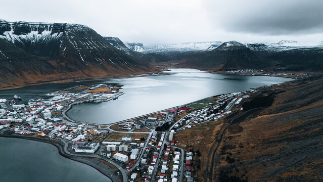Aerial view of a town nestled on the edge of a tranquil fjord, where buildings meet the water's edge under a sky heavy with clouds, Isafjordur, Iceland.
