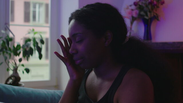 African American woman sitting on couch showing fear and emotional distress, touching face while struggling with inner turmoil, anxiety, and unresolved trauma in quiet home environment
