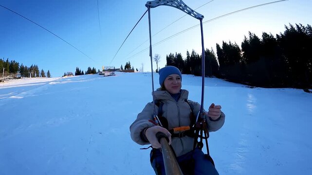 A smiling woman records her flight on an extreme zipline above a snowy mountain slope in Bukovel resort. Concept of adrenaline, winter adventure, and outdoor recreation.