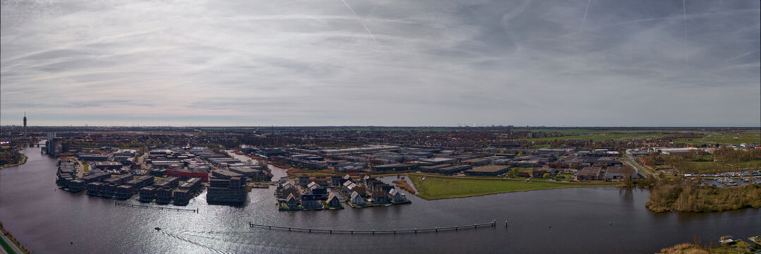 Aerial view of a tranquil waterfront community with modern houses and shimmering waterways under a soft, diffused light, Zaanstad, Noord-Holland, Netherlands.