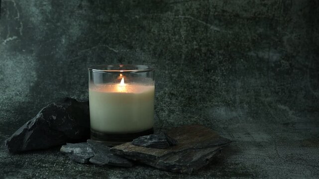 nice burning luxury aromatic scented candle glass is on stone table with a few rocks and background of grey stone wall in bed room to create relax and romantic moment for lovers on Valentine day