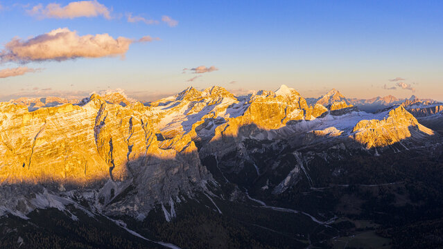 Aerial view of majestic Dolomites mountains draped in golden sunlight meeting the cool shadows, a breathtaking display of nature's artistry, Badia valley, Italy.