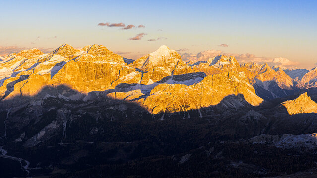 Aerial view of golden light washing over the Dolomites peaks of the rugged mountains, casting dramatic shadows across the landscape, Badia Valley, Veneto, Italy.