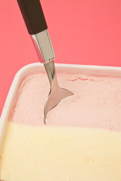 Close-Up of a spoon in a tub of Neapolitan ice cream in front of a pink background