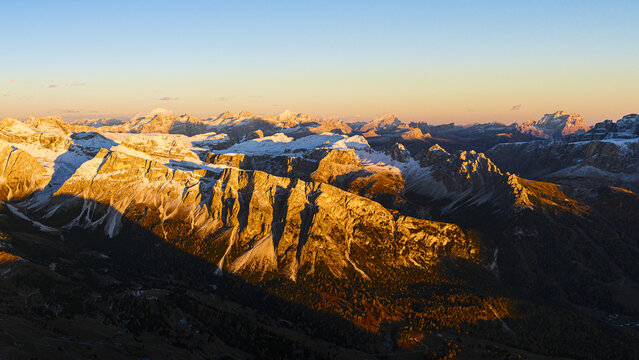 Aerial view of the majestic Seceda Gardena Valley Dolomites, painted in the fiery hues of dawn, where jagged peaks meet soft snow under a vast, pale sky, Trentino-South Tyrol, Italy.