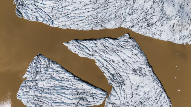 Aerial view of glacial ice formations float in the muddy waters of Hoffellsjokull, creating a striking contrast between the stark white ice and the earth-toned water, Hoffellsjokull, Iceland.