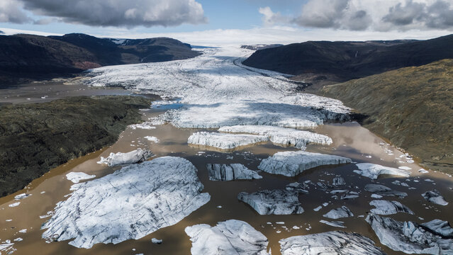 Aerial view of icebergs adrift in the glacial lagoon, carved by time and weather, against a backdrop of stark mountains, Hoffellsjokull, Iceland.