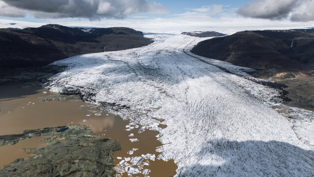 Aerial view of glacial ice flowing into a silt-filled lake under a cloudy sky, Hoffellsjokull, Iceland.