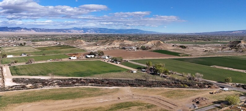 Aerial view of verdant fields meet arid landscapes under a vast blue sky, contrasting the textures of rural life, Fruita, Colorado, United States.