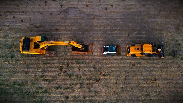 Aerial view of heavy machinery, including an excavator, a dump truck, and a bulldozer, standing in a field of dry grass, Fruita, Colorado, United States.