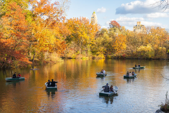 Manhattan, United States - 08 November 2025: View of rowboats gently gliding across the serene lake in Central Park, framed by the vibrant autumn foliage and the iconic city skyline.