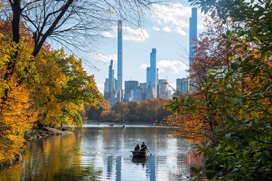 Manhattan, United States - 08 November 2025: View of Central Park's tranquil lake reflecting fall colors, framed by vibrant foliage and the iconic city skyline.