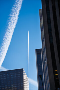 Manhattan, United States - 03 December 2025: View of skyscrapers piercing the crisp blue sky, bisected by contrails forming ephemeral white lines against the urban landscape.