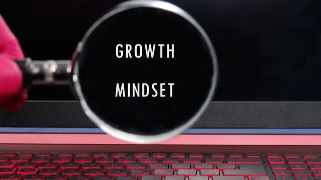A close up view shows a hand holding a magnifying glass bringing the text Growth Mindset into sharp focus on a desk