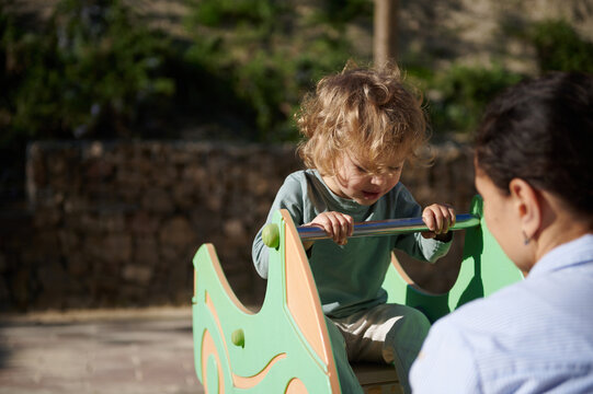 Toddler Playing on Seesaw at Outdoor Playground With Parent Supervising in Sunny Park