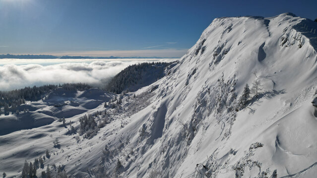 Aerial view of a snow-covered mountain peak piercing through a sea of clouds under a crisp blue sky, Gingins, Vaud, Switzerland.