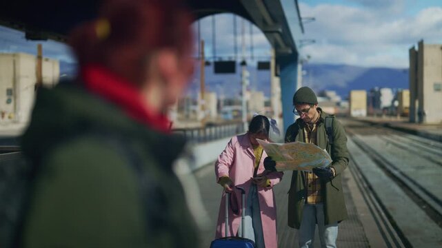 A man and woman, tourists, consult a map and a phone for directions on a train station platform. A couple navigates their journey, examining a map and mobile device while waiting for a train.