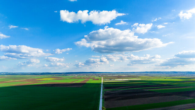 Aerial view of patchwork fields in vibrant greens and browns under a vast sky with fluffy clouds, Kovilj, Vojvodina, Serbia.