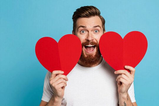 Man holds giant red heart with joyful, surprised expression.