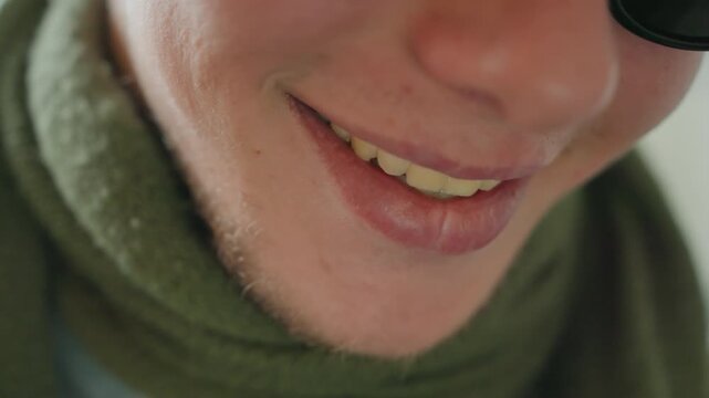 Smiling white man showing warm laugh with green scarf and sunglass closeup, cheeky grin revealing teeth, candid joyful vibe, cozy indoor light, playful approachable narrator energy