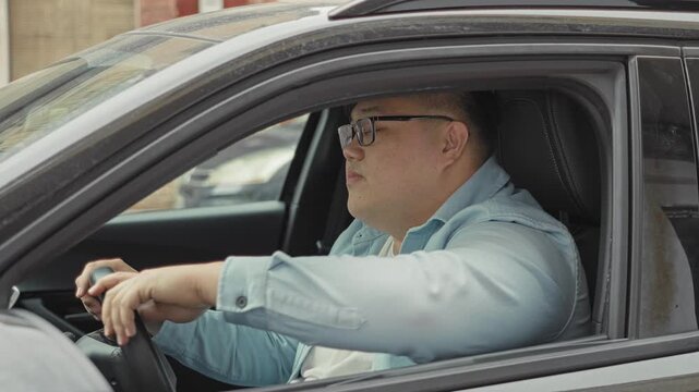 Man in parked car grips steering wheel, rests arm on door, glances forward and rubs forehead at street; frustration pause.