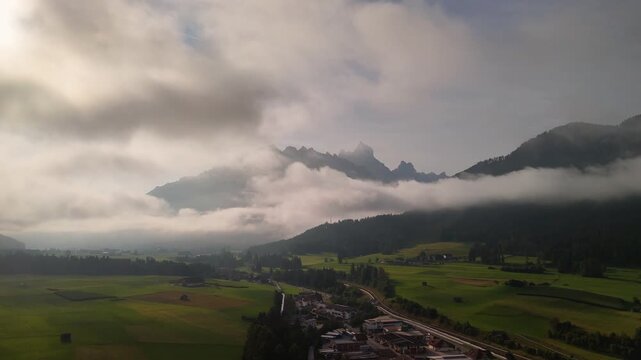 The mountains and peaks of the Sexten Dolomites are surrounded by heavy clouds in the morning light. A drone view from the valley out into the alpine landscape. 