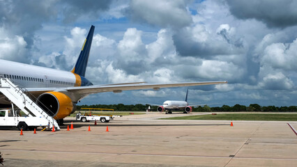 Naklejka premium Airplanes parked on tarmac at an airport with a staircase leading to the cabin and clouds in the blue sky, showcasing aviation infrastructure and operations