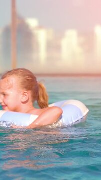 Joyful moments in a sunny pool where a little girl splashes and swims with her bright floatie in a vibrant city backdrop