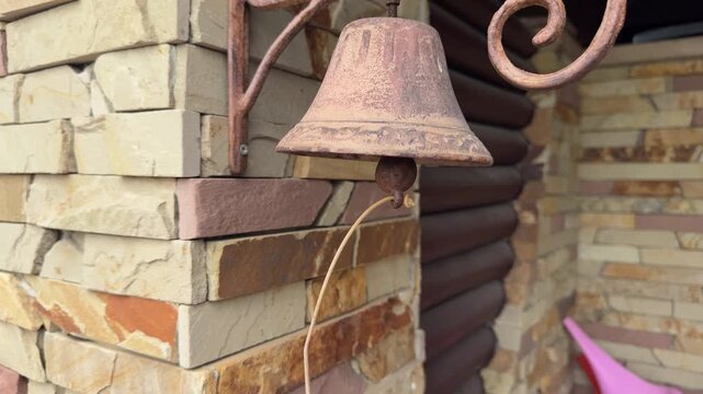 Decorative antique bell fixed on coarse stone wall with frayed rope