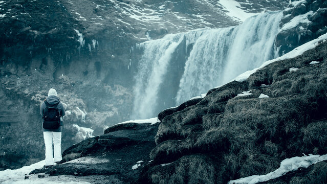 Rear view of a young Woman in warm clothing standing in front of Skogafoss waterfall on a winter day, Iceland