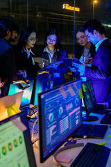 Obraz premium Successful technical specialists brainstorming and reviewing digital strategy at night. Professional managers supervising international business growth and IT operations in a modern neon office.
