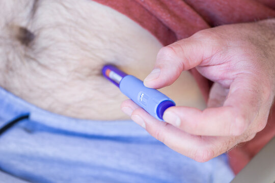 man performing a subcutaneous medical injection using a blue injector pen Ozempic into his belly for weight management and blood sugar control in an indoor environment concept of medical treatment