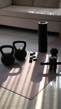 Home workout equipment set including kettlebells, ab roller, and foam roller on yoga mat with morning sunlight shadows for fitness and wellness concept