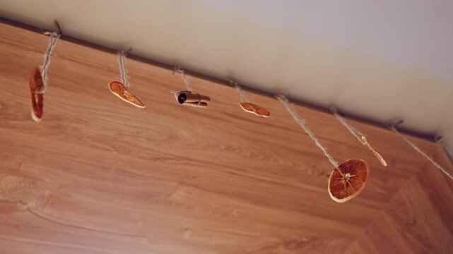 Dried orange slice garland hanging over wooden corner with string light clips, rustic boho decoration for cozy autumn harvest, warm amber tones, textured wood floor, handmade DIY craft, closeup