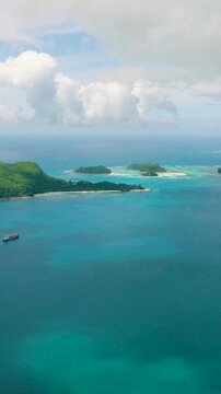 Ocean with a ship and a green island in the distance under a partly cloudy sky. Seychelles, Mahe. Ile au cerf island.