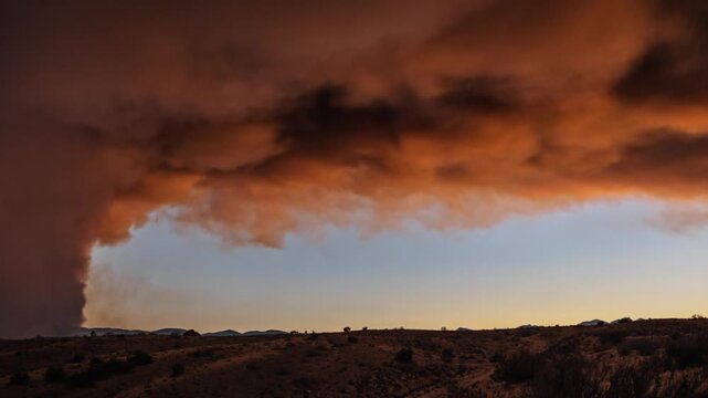 Dramatic smoke cloud from a wildfire billows across the sky above a desert landscape
