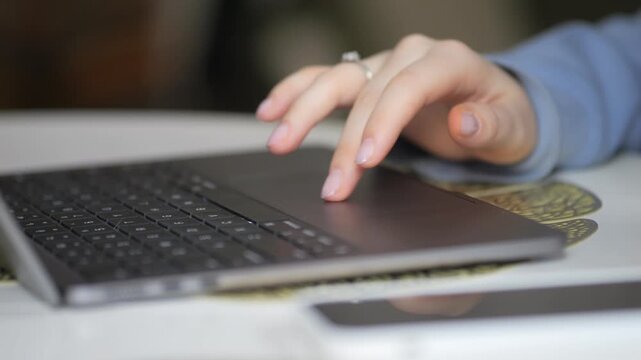 Close-up of a person's hand using a laptop. Fingers tap on keyboard and touchpad. Hand moves smoothly over laptop surface. Background slightly blurred for focus on action. No animals or plants visible