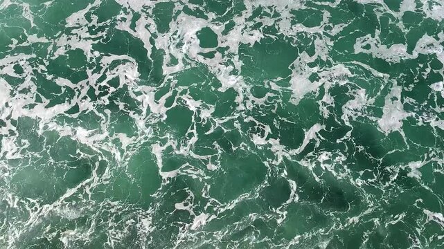 At Sea - Aerial view of foamy waves creating interesting abstract patterns in deep turquoise water. Swirling white foam contrasts emerald ocean texture at open sea.