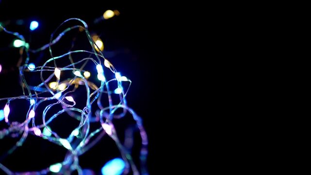 A close-up of colorful LED string lights blinking rapidly against a pitch-black background. Concept of festive holiday celebrations, magical party atmospheres, and abstract energy.
