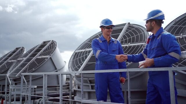 Two technicians handshake near cooling towers at industrial plant