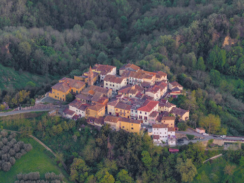 Aerial view of the small hilltop village with terracotta roofs and a church tower surrounded by dense green forest and olive groves in Piantravigne, Tuscany, Italy.