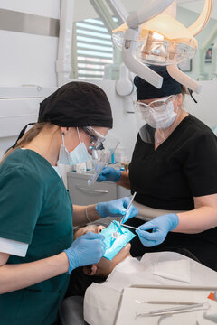 Professional dentist and assistant applying composite material from syringe to patient tooth with single-use microbrush. Restorative dentistry procedure with rubber dam in modern stomatology clinic.