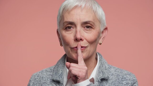 Senior woman making silence or shh gesture on pink